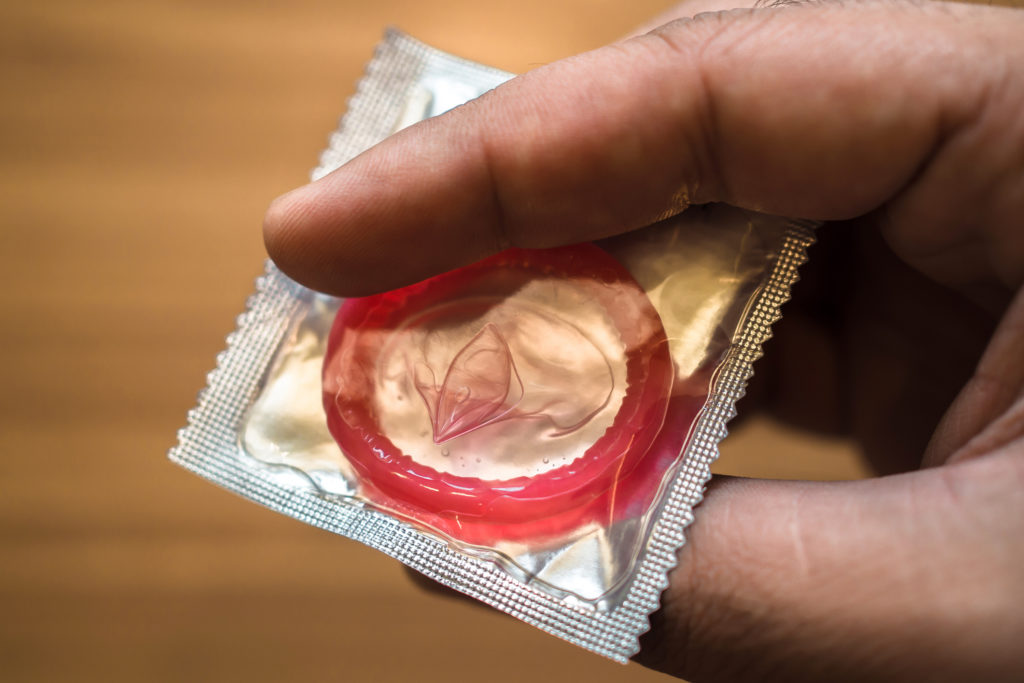 sealed condom in hand on wooden background